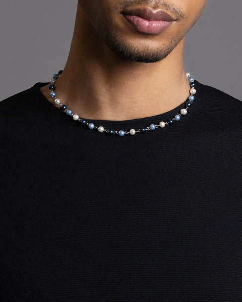 A men wearing the FIVE JWLRY pearls necklace made with 2 shades of blue glass beads and white pearls, crafted with natural shell. 45cm + 5cm extension, rollo chain for adjustment. Fashion accessory, statement jewelry. Designed in Montreal, Canada.
